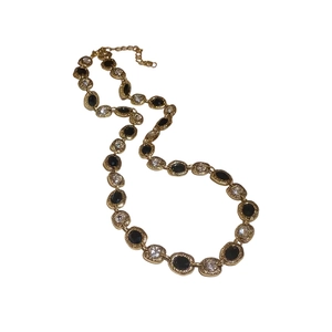 Collier vintage doré avec pierres noires ovales et cristaux sur un fond blanc pur