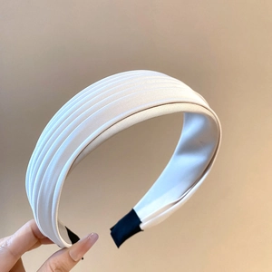 Gros plan sur le serre-tête en satin plissé blanc crème montrant la texture du tissu