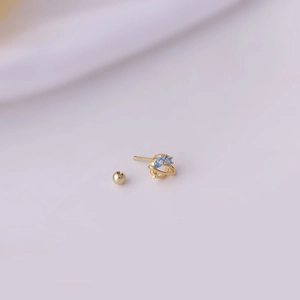 Titanium steel planet stud earring with gold finish and blue zircon stones on purple fabric