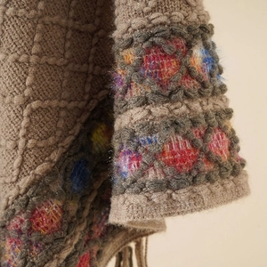 Close-up of diamond pattern knit poncho with colorful yarn details and fringe edge