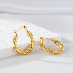 Detailed macro view of gold-plated knotted twisted rope hoop earrings on a stone base