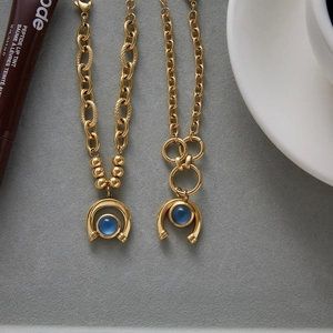 Close-up of 18K gold stainless steel equestrian chain bracelet with blue resin horseshoe pendant