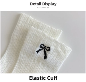 Detail of white ribbed cotton sock featuring elastic cuff and black bow embroidery