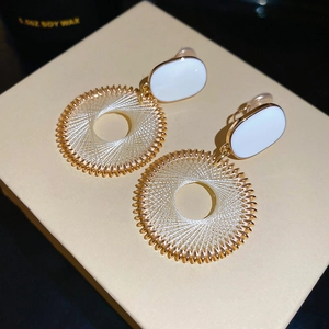 Detailed shot of golden dreamcatcher earrings with white oval accents on a gift box