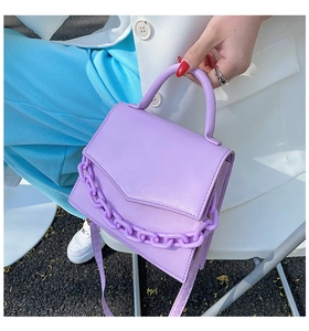 Detail of purple crossbody bag with chunky plastic chain handle held by a model