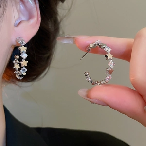 Close-up of geometric C-shaped earrings with sparkling star and square zircons