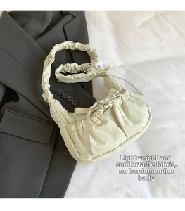 Detail of light beige pleated shoulder bag featuring adjustable bow straps and ruched fabric