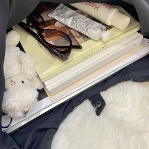 Internal storage of a large black tote bag showing books, glasses, and plush charm