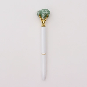 Detail van witte metalen balpen met ruwe groene kristalsteen en gouden klauwzetting