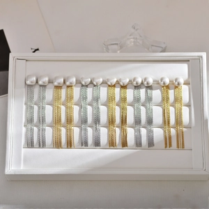 Detail view of 6 pairs of pearl tassel earrings in gold and silver on white leather tray