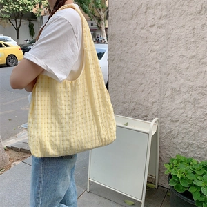 Close-up of vibrant yellow textured plaid canvas tote bag worn by a model in sunlight