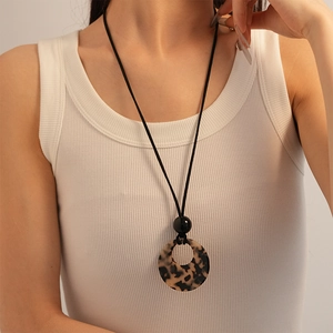 Close-up of a leopard print resin ring pendant on a black cord necklace with a ribbed vest
