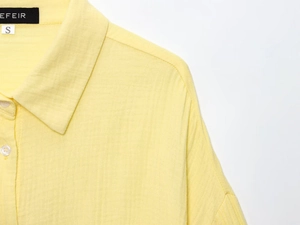 Detailed close-up of yellow cotton linen shirt collar with white buttons and brand tag