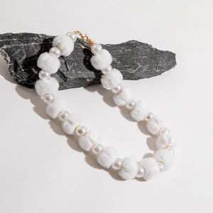 Détail du collier avec perles blanches, pompons en peluche et fermoirs dorés