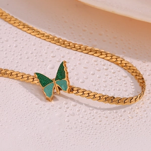 Macro shot of a gold butterfly pendant with teal and green enamel on a Cuban link chain