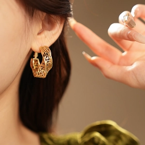 Close-up of golden geometric hollow twist hoop earrings worn by a female model