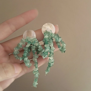 Detail of flower tassel earrings featuring white mother-of-pearl and green stone droplets