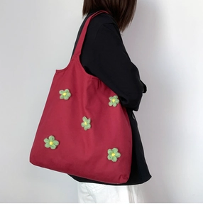 Side view of a large red canvas tote bag with a green flower applique on a model