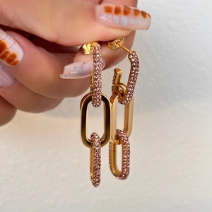 Detailed view of long gold chain earrings with pink cubic zirconia held in hand