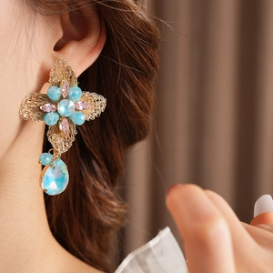 Close-up of vintage flower earrings with blue and pink crystals on gold woven metal