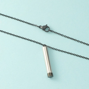 Detail view of silver cylindrical pendant with black chain on light blue background