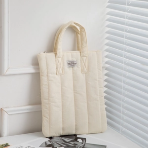 Close-up of cream quilted laptop sleeve with vertical stitching and vintage label detail