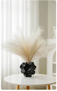 Close-up of a modern black sculpted ceramic vase with fluffy beige pampas grass on a table