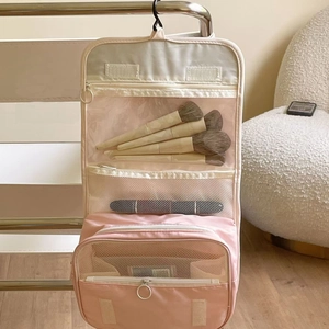 Pink hanging toiletry bag with embroidery showing inner compartments and makeup brushes