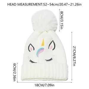 Détail du bonnet blanc en tricot avec broderie licorne et pompons arc-en-ciel colorés
