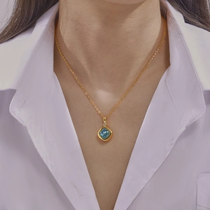 Elegant gold necklace with a blue square gemstone pendant worn by a model on white shirt