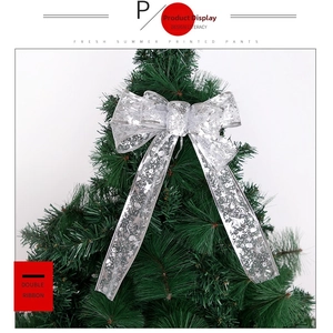 Close-up of double-layer silver Christmas ribbon bow with snowflake patterns on pine branch