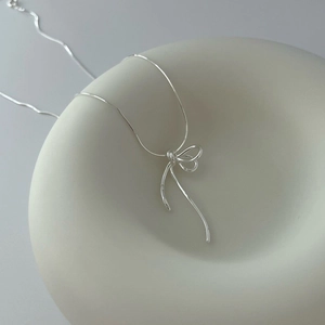 Minimalist S925 sterling silver ribbon bow necklace on matte ceramic tray