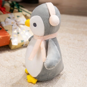 Close-up of cute plush penguin doll with pink scarf and earmuffs on a soft rug