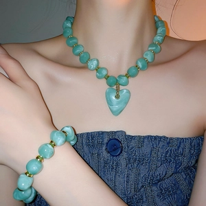 Close-up of mint green heart necklace and beaded bracelet with gold accents on model