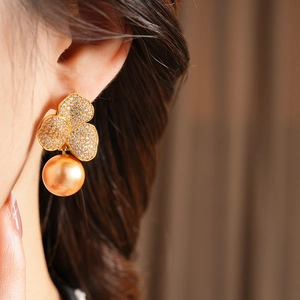 Detail of gold flower earrings with pavé crystals and a hanging gold pearl drop