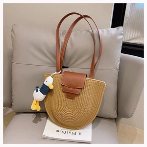 Detail of semi-circular woven cotton straw tote bag with brown leather strap and duck charm