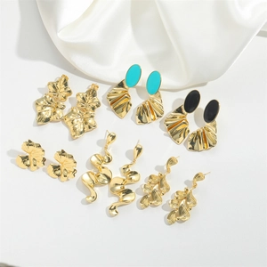 Macro shot of gold-plated maple leaf earrings and wave-pattern enamel studs on white silk