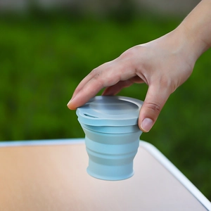 Portable light blue collapsible silicone cup held outdoors for travel and camping use