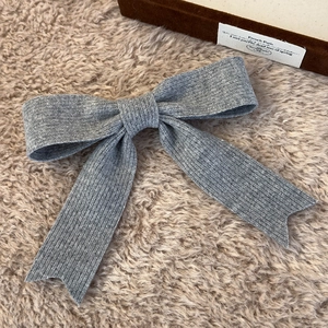 Detail of grey knitted bow hair clip with textured ribbed fabric on plush background