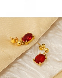 Gros plan sur des boucles d'oreilles dorées avec grands zircons rouges rectangulaires