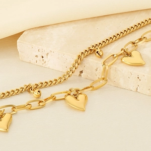 Detail of 18K gold-plated double-layer bracelet with heart charms and beads on travertine