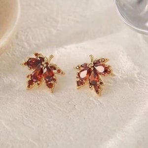 Vue macro de boucles d'oreilles feuille d'érable dorées avec cristaux rouges taille poire