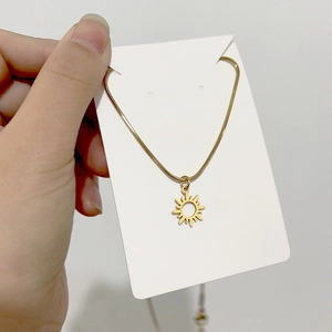 Detail of 18K gold-plated snake chain necklace with sunburst pendant on a white card