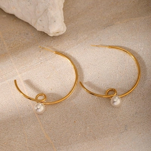 Minimalist C-shaped twisted gold earrings with hanging white pearl on stone surface