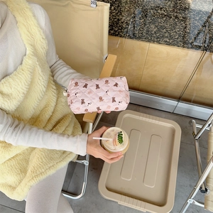 Pink quilted cosmetic bag with brown bear pattern held outdoors in a lifestyle setting