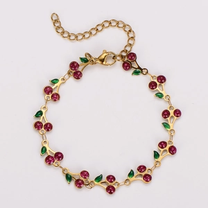 Close-up of bohemian gold cherry bracelet with red crystal charms and green enamel leaves