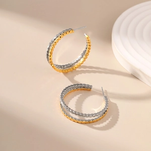 Detail of gold and silver two-tone layered hoop earrings with textured honeycomb finish