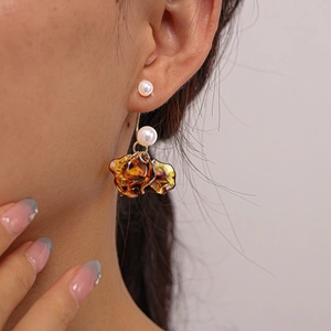 Detail of amber acrylic flower petal earrings with hanging pearls shown on a model