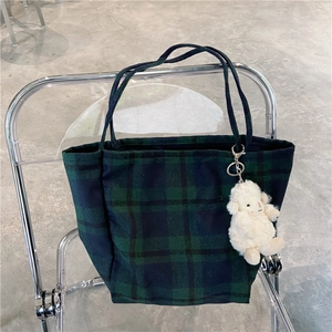 Close-up of green plaid tote bag with sheep pendant on transparent chair