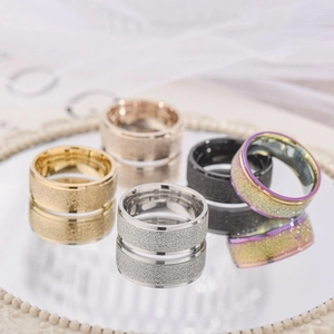 Set of frosted titanium steel rings in gold, silver, and black on a mirrored surface